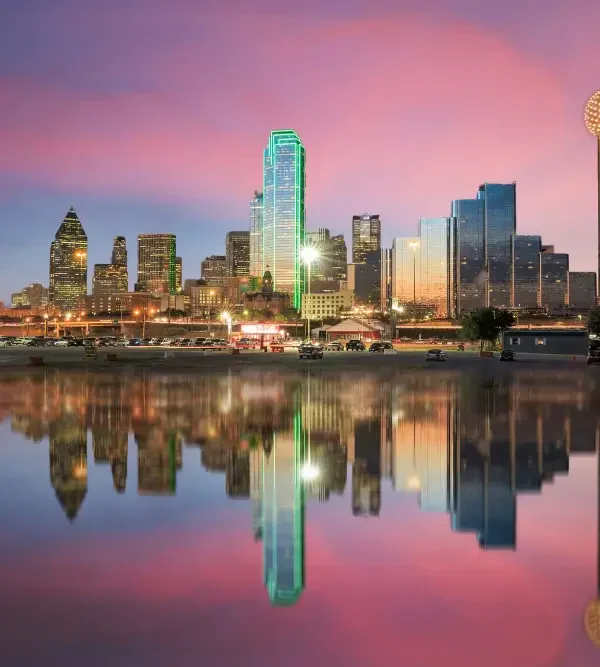 Dallas skyline shimmering at dusk, reflecting on calm water under a vibrant pink and purple sky, highlighted by illuminated buildings.